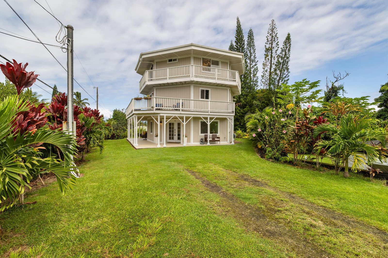 Front elevation of the octagonal tri-level home above a lawn bordered with red ti