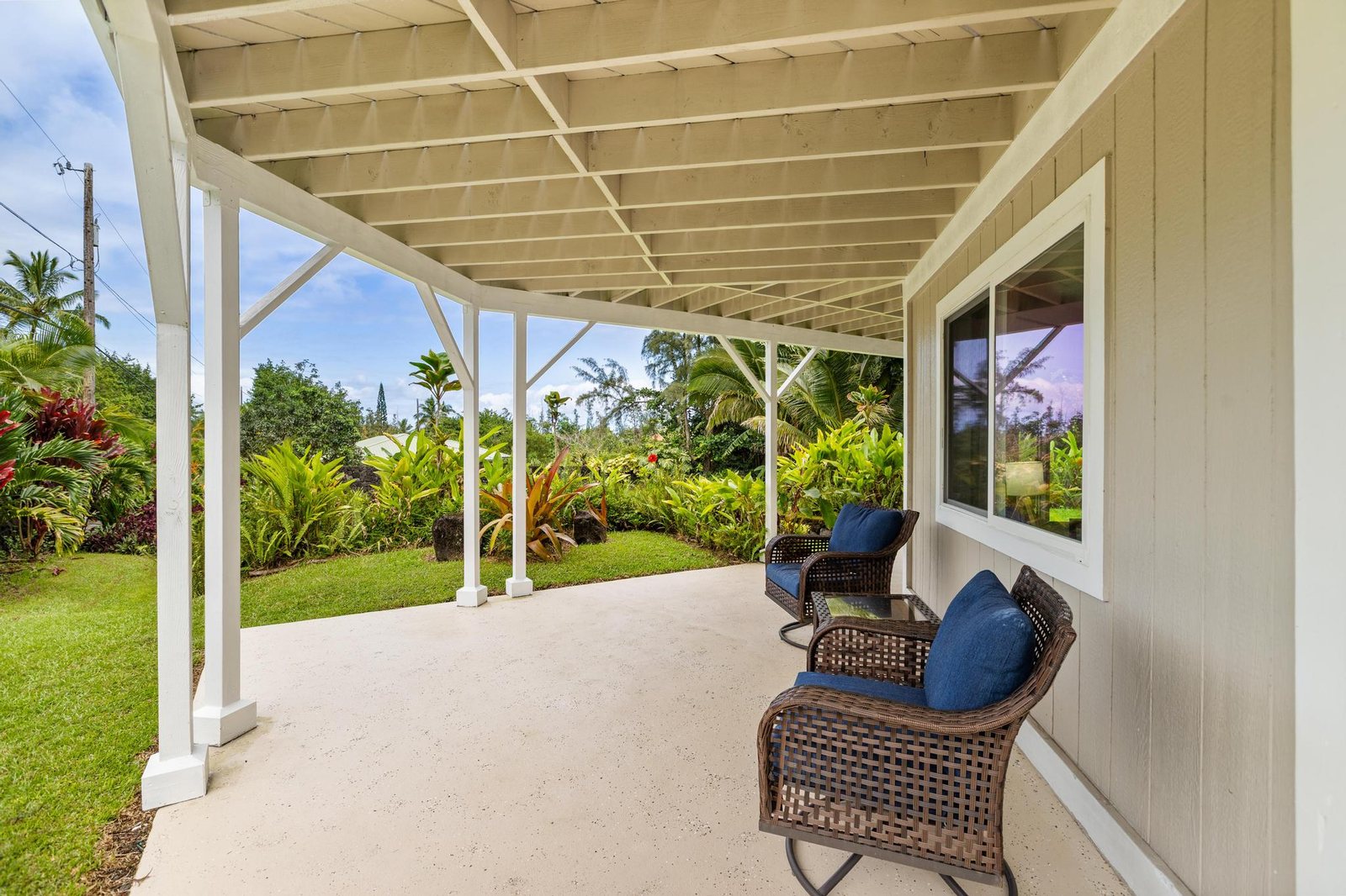 Covered garden-level lanai with wicker seating looking onto lawn and tropical planting