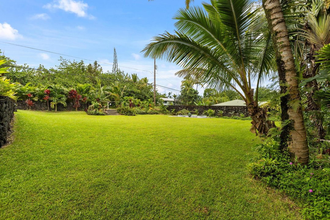 Wide lawn bordered by palms and a lava-rock wall