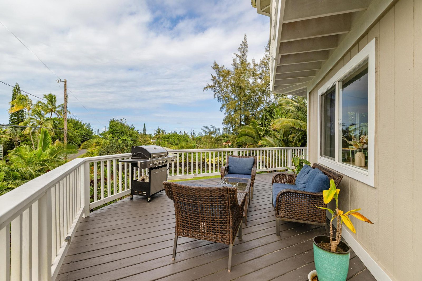 Furnished upper wraparound lanai with wicker seating and grill overlooking the garden