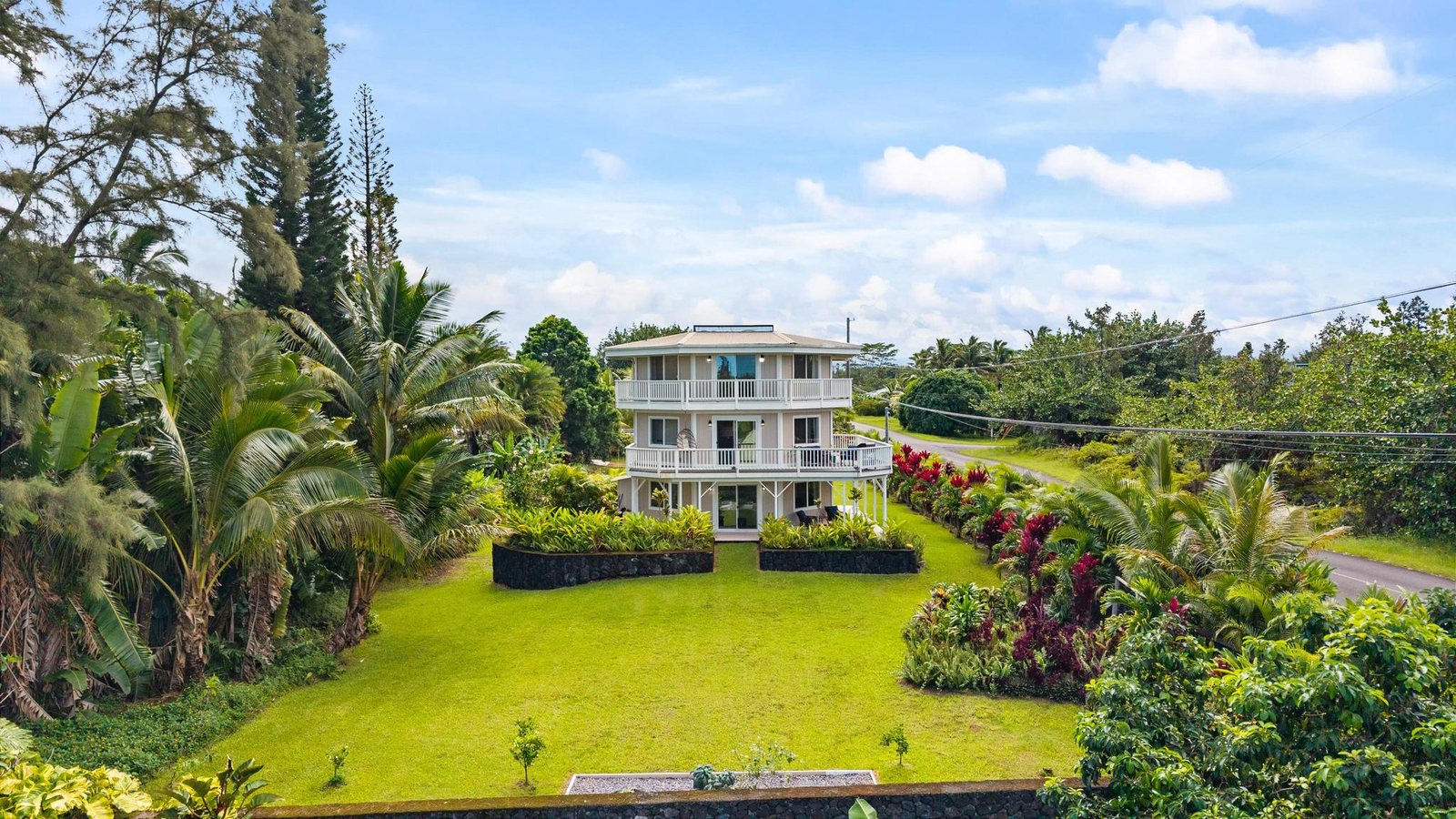 Aerial view down a long lawn framed by palms to the three-level octagonal home