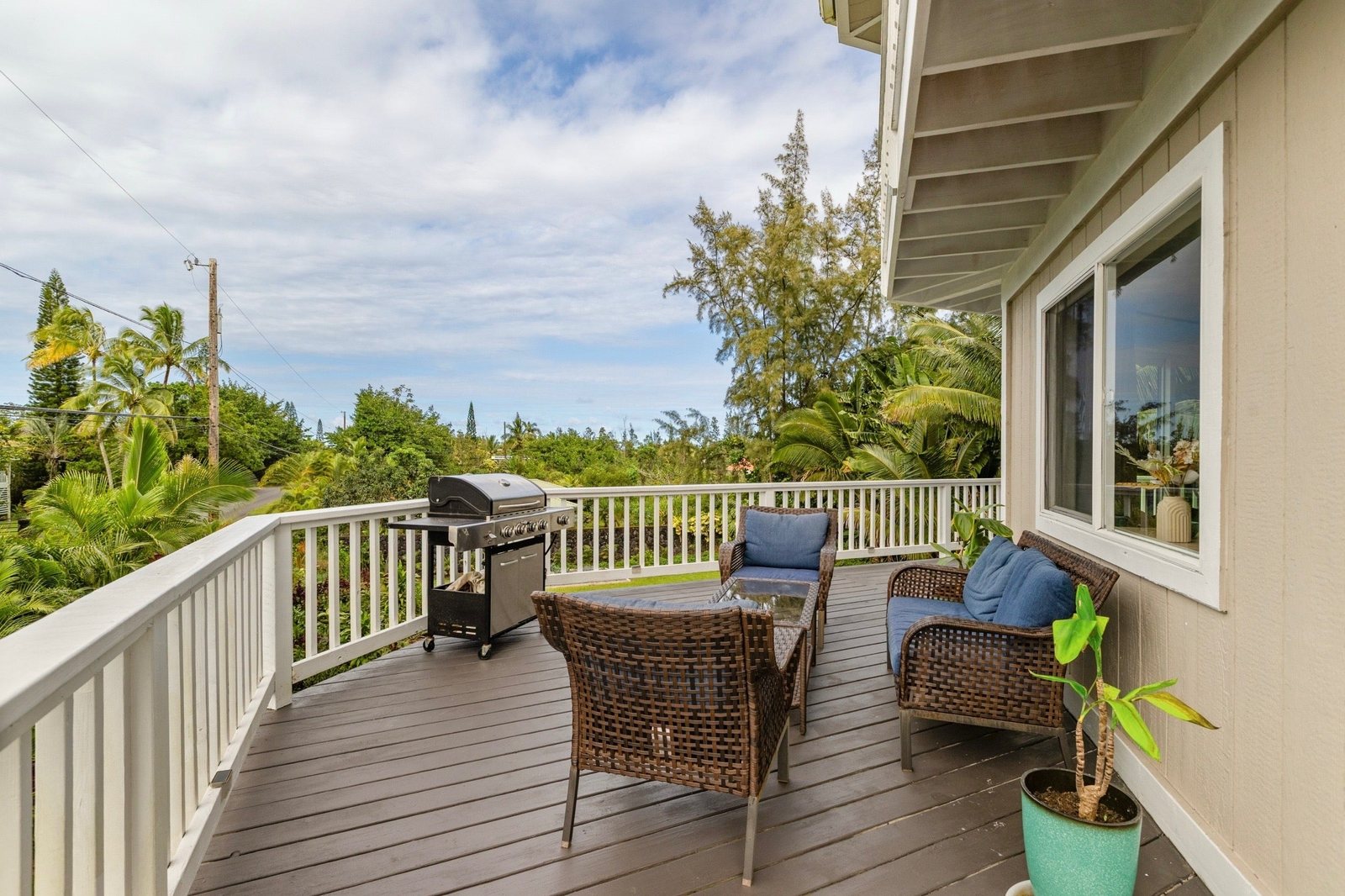 Furnished upper wraparound lanai with wicker seating and grill overlooking the garden