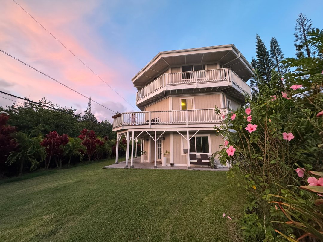 The house beneath a pink and violet sky at dusk, with hibiscus in the foreground